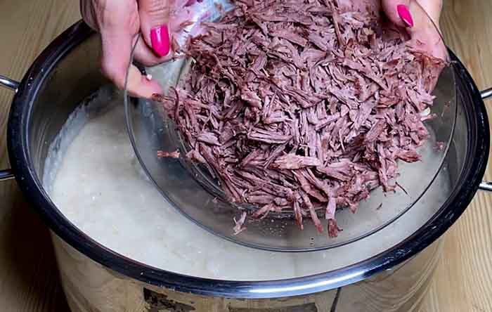 Shredding cooked mutton by hand to create a stretchy texture for Iranian Haleem